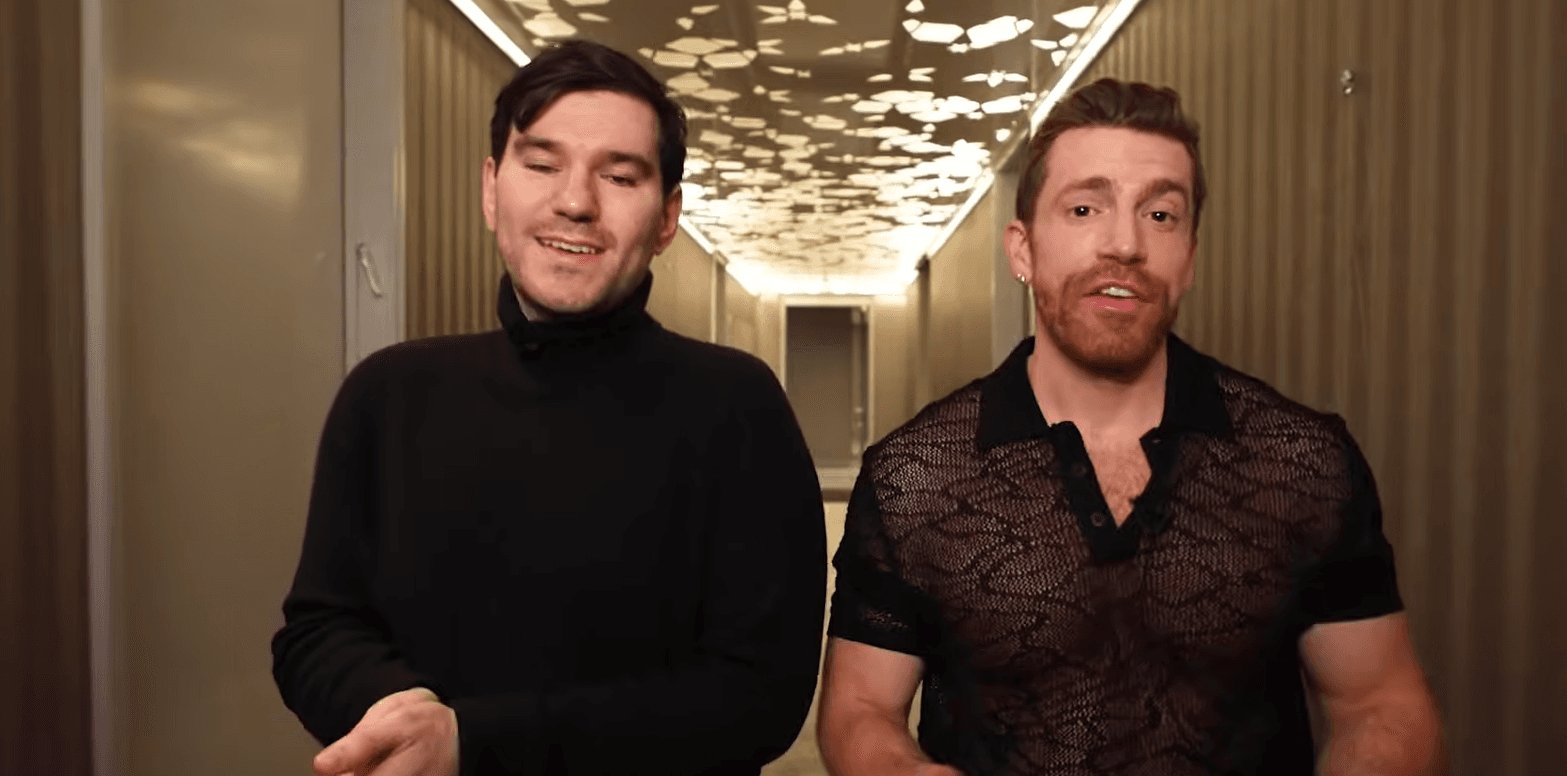 Reality stars posing together at a colorful outdoor event, wearing stylish outfits with bright lights in the background.