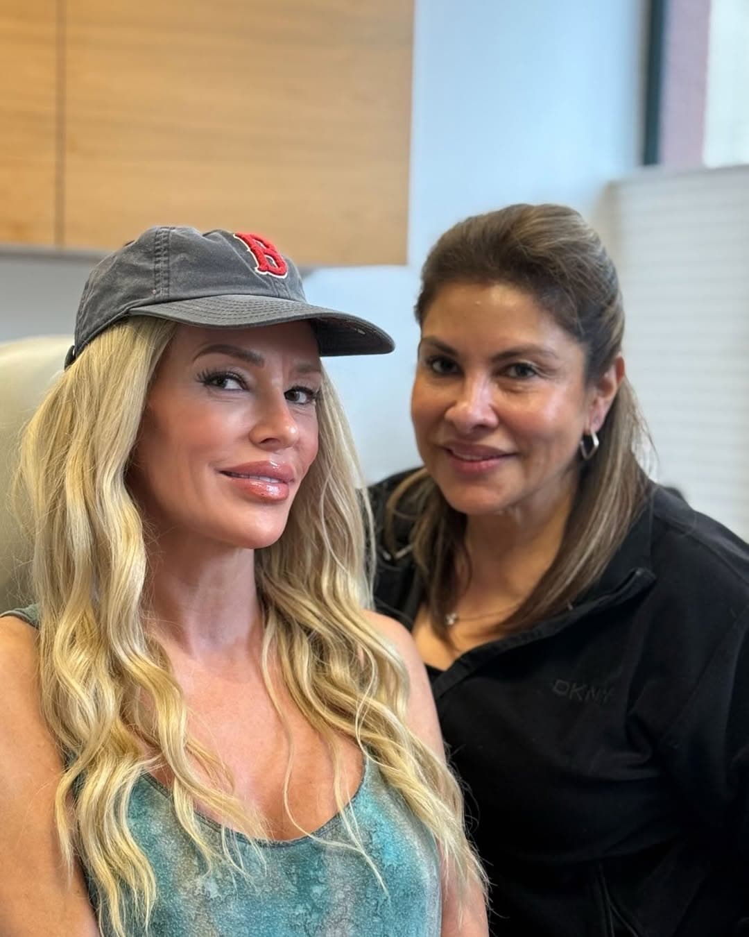 Brandi Glanville sitting in a bright room, wearing a white top and stylish sunglasses, looking thoughtfully at the camera.
