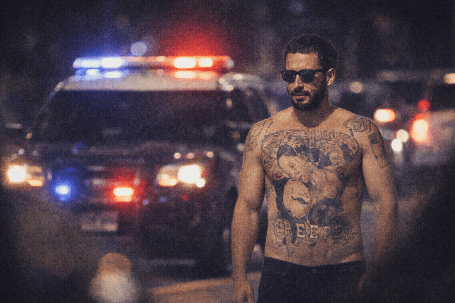 Shia LaBeouf wearing a colorful Mardi Gras mask and beads, being escorted by police officers in a crowded street.