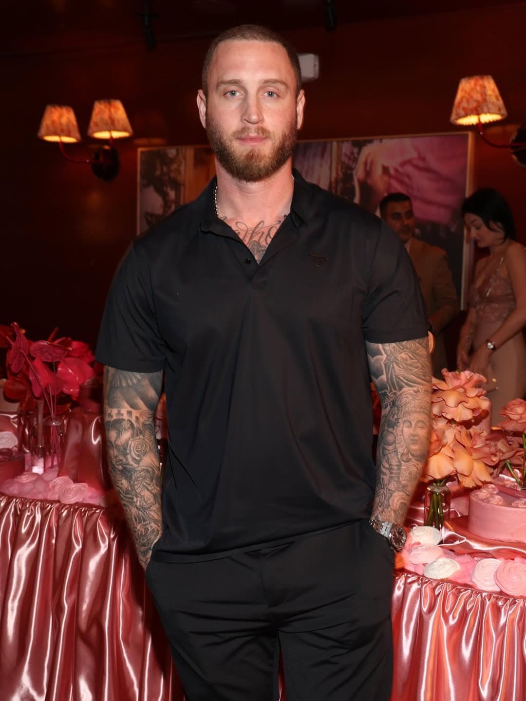 Chet Hanks sitting on a luggage cart at an airport, wearing a casual white t-shirt and cargo shorts, looking frustrated.
