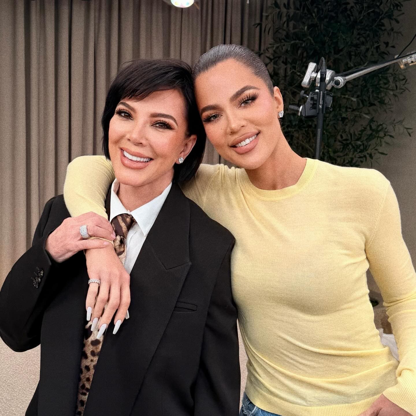 Khloé Kardashian sitting on a couch in a casual outfit, looking thoughtfully at a baby toy in her hands.