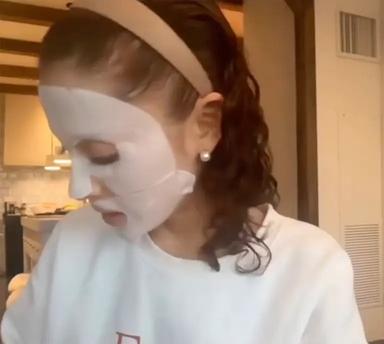 Ariana Grande showcasing her natural curls, wearing a casual white top and sitting in a cozy, well-lit room.