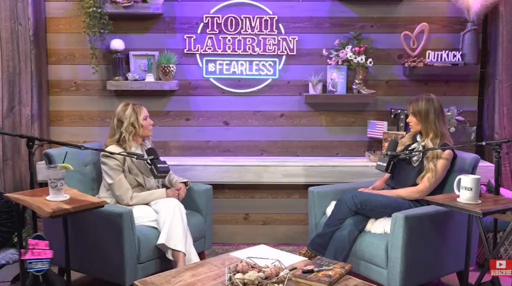 Kathie Lee Gifford sitting on a talk show set, wearing a red blouse, smiling and gesturing with her hands.